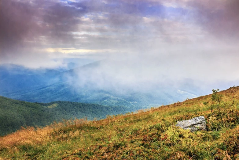 clouds are rolling through the valley on top of a mountain