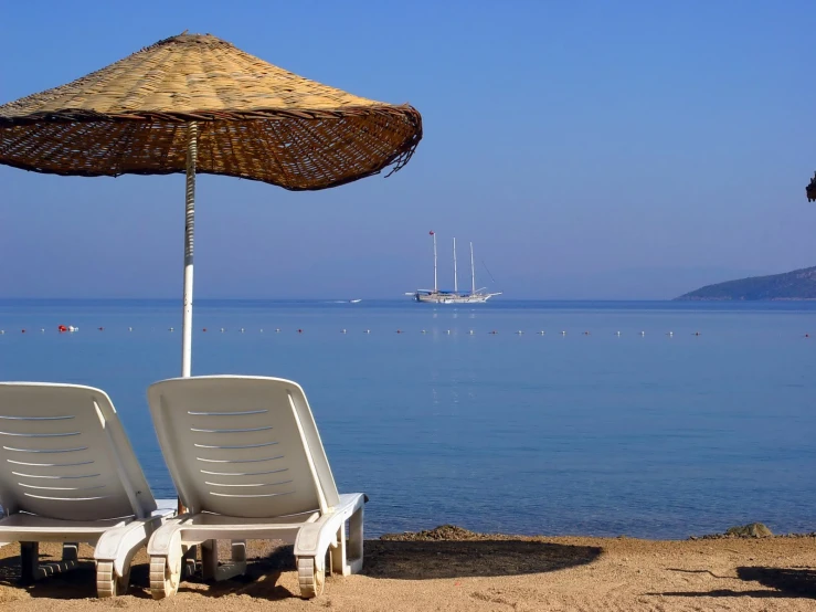 two chairs sit on the sand near a parasol