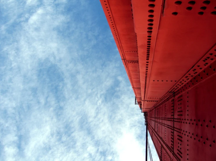 the underside view of an orange bridge with a white cloud in the blue sky