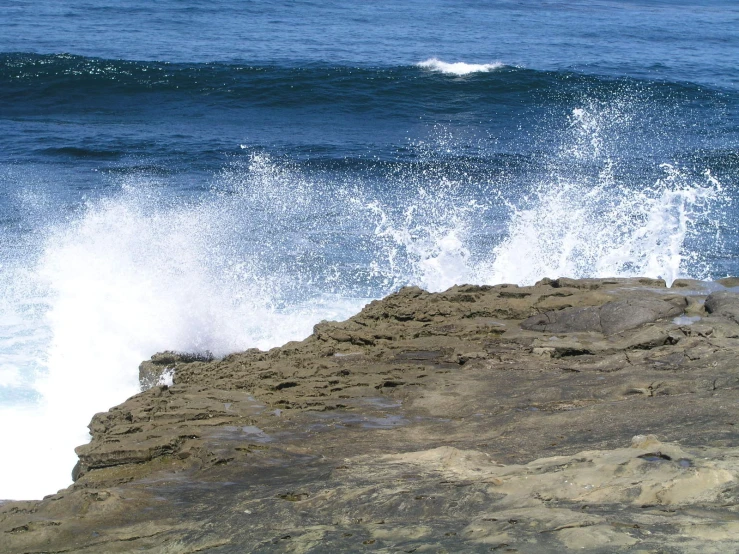 the crashing wave on top of the rocky shore