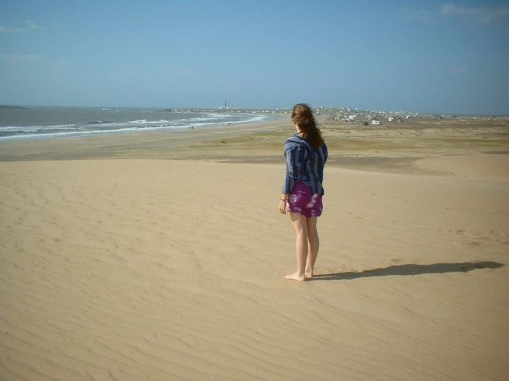 a young woman in purple stands on the beach and looks out at the ocean
