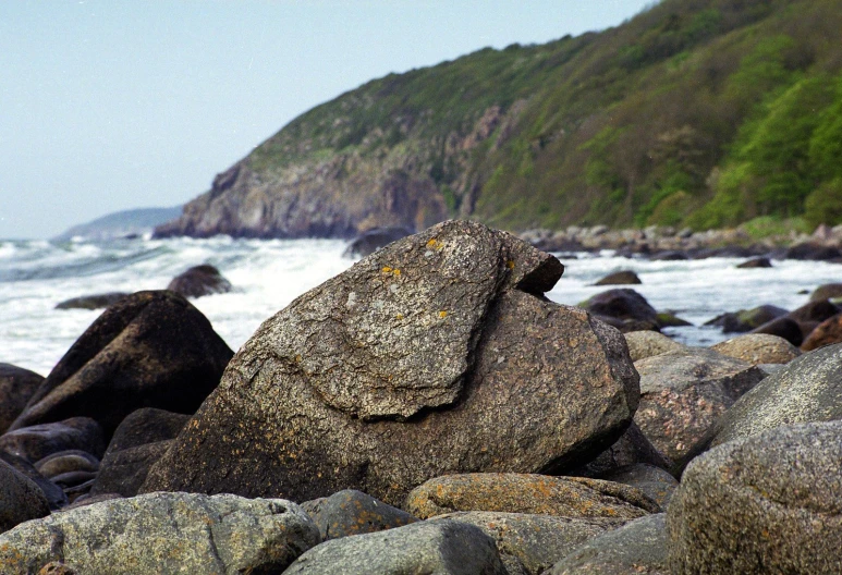 rocks on the beach have faces of mountains in the background