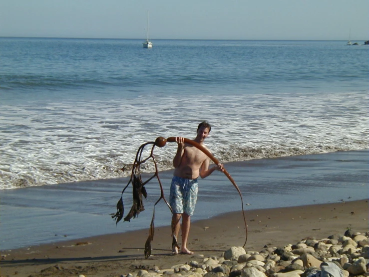 a young man is walking along the beach holding a hoe
