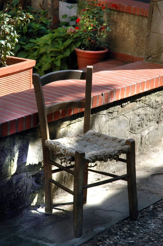 an old wooden chair sitting on top of a sidewalk next to flowers