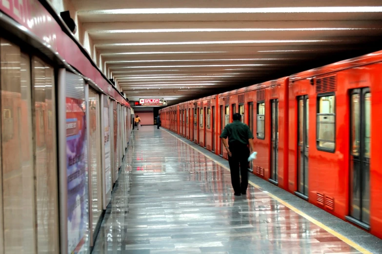 a long red train with a guy walking on the side of it