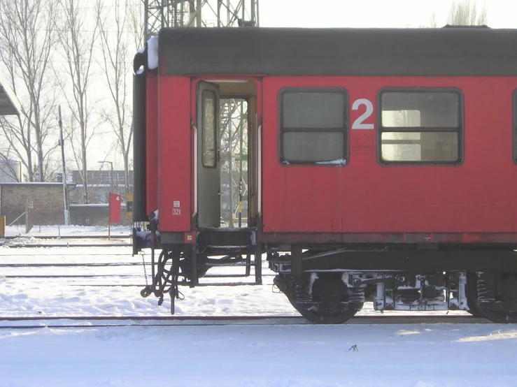 a red train car sitting on the tracks next to snowy ground