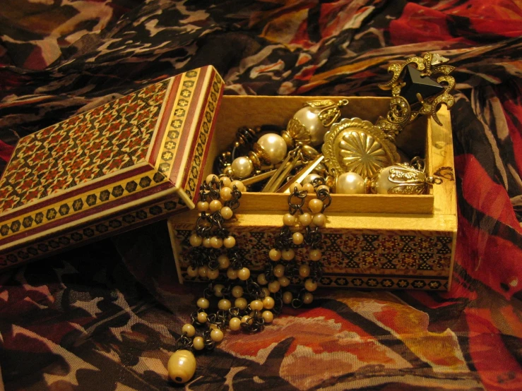 a box on a bed is filled with many necklaces and a book