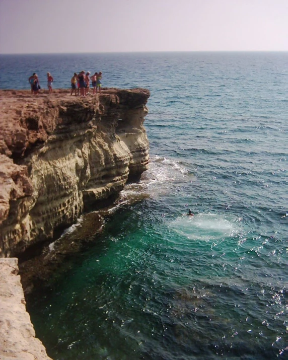 a cliff with people on the edge overlooking the ocean