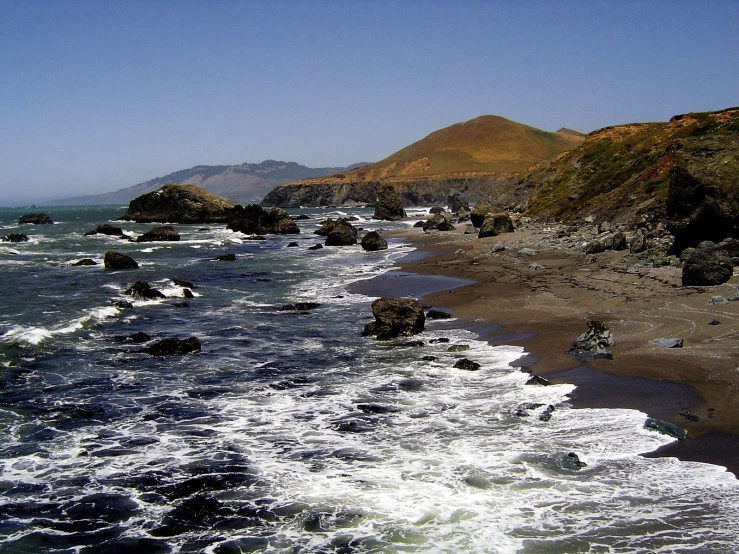 waves breaking onto the shore with two mountains in the background