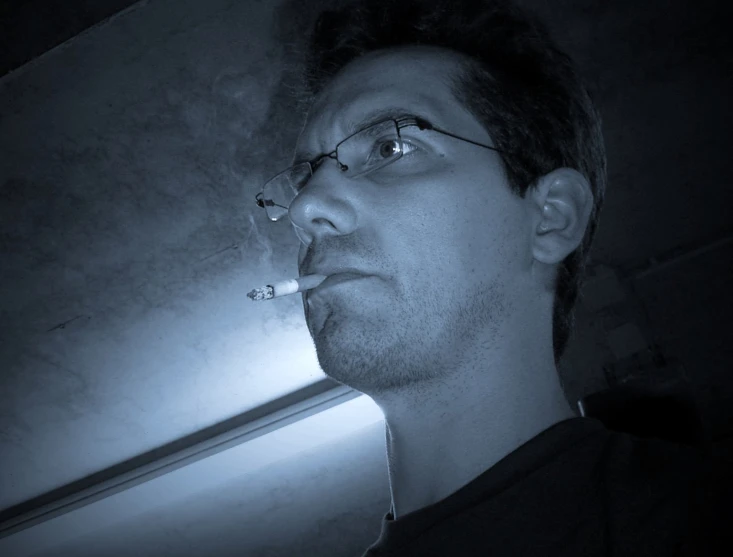 man in glasses smoking a cigarette in the dark