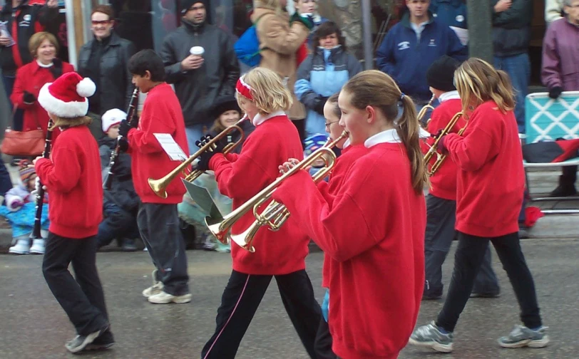 a bunch of children in christmas clothes are marching down the street