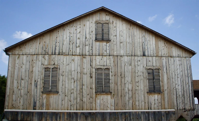 a weathered wood barn with shutters on each side and a sky background