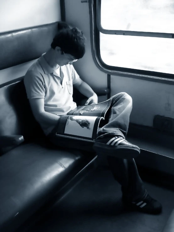 a man in white shirt sitting on train holding a magazine