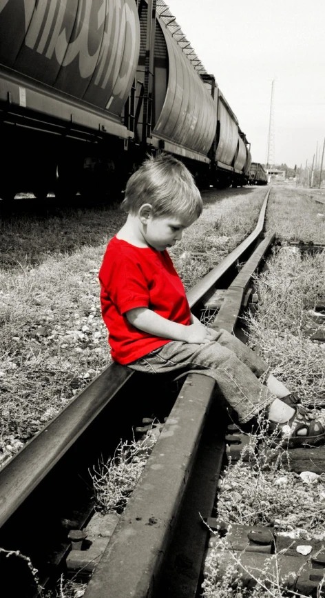 little boy sitting on railroad track in black and white