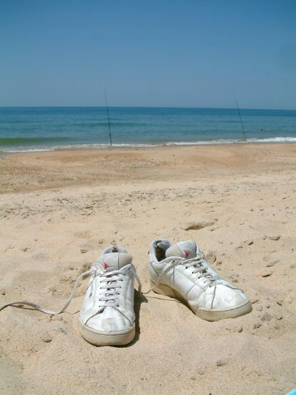 pair of white shoes resting on sandy beach near ocean