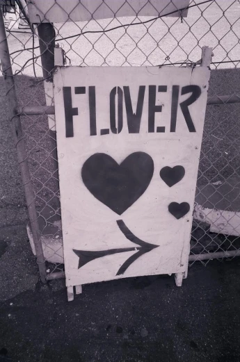 a sign with a heart and the words flower is attached to a chain link fence