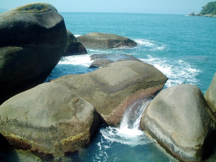 rock formation with waves running by on blue water