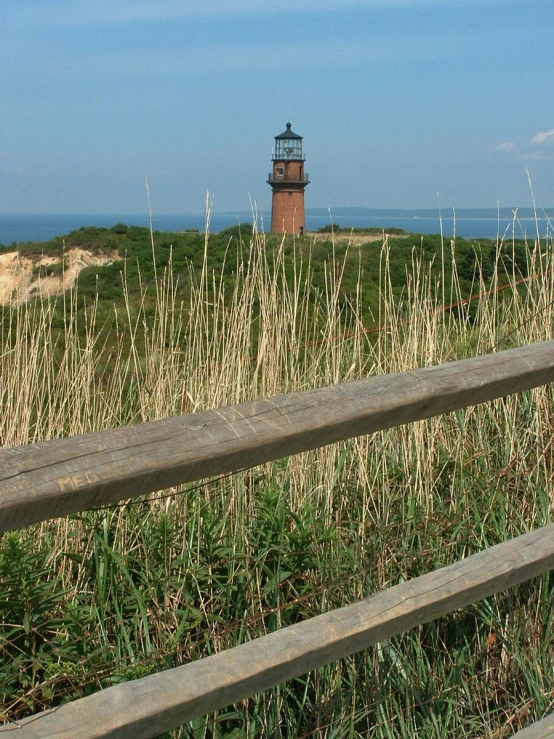 a wooden fence overlooks a grassy beach and lighthouse