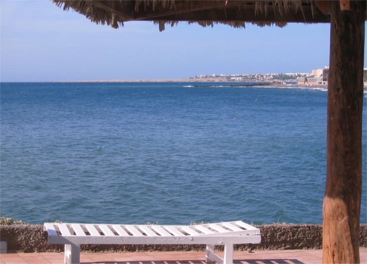 an empty bench near some blue water on a beach