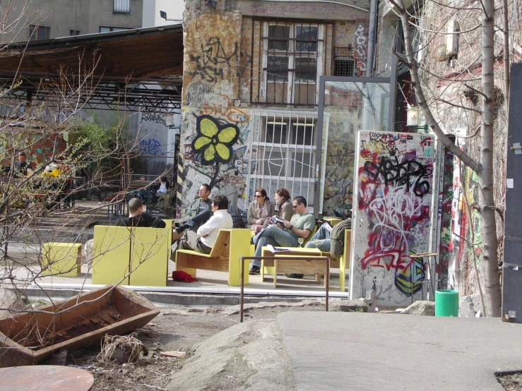 people sit on yellow benches with graffiti in an industrial area