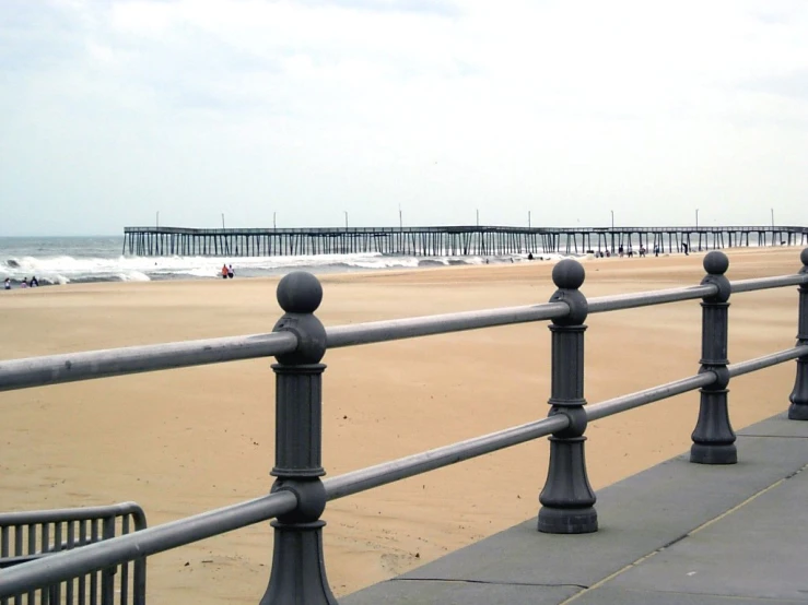 a walkway going to the beach, with a long wooden pier in the distance