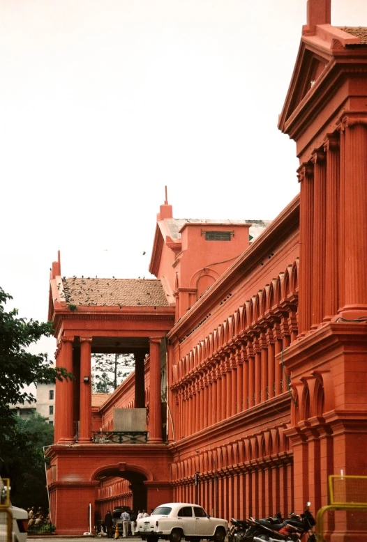 an orange building with a tall archway between two rows of parked cars