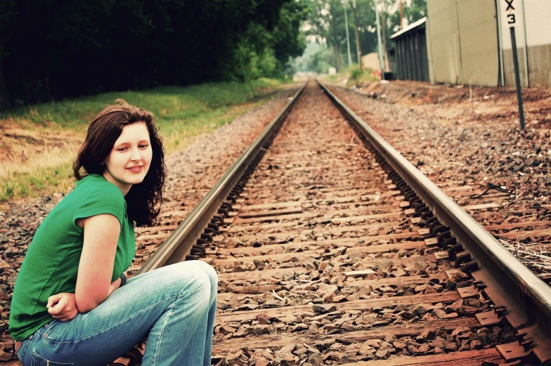 a girl sitting on some tracks in a green shirt