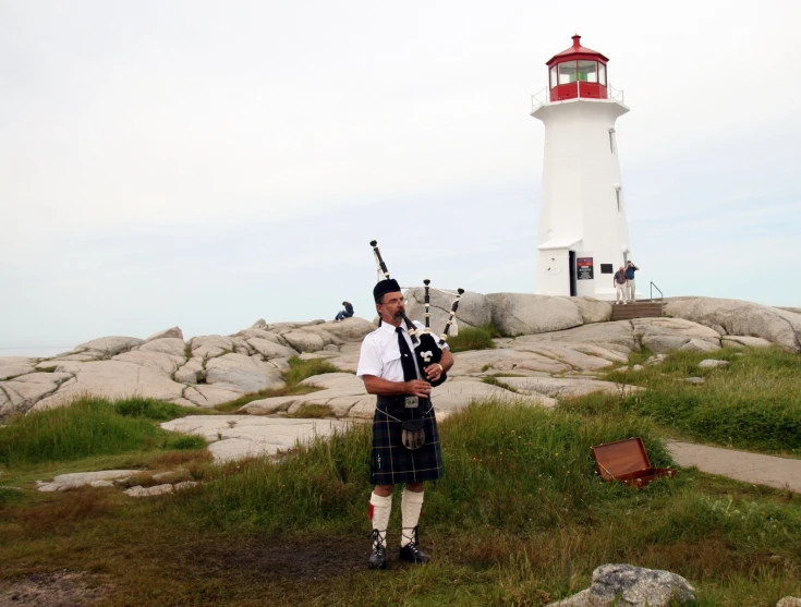 the bagpipe player stands in front of a light house