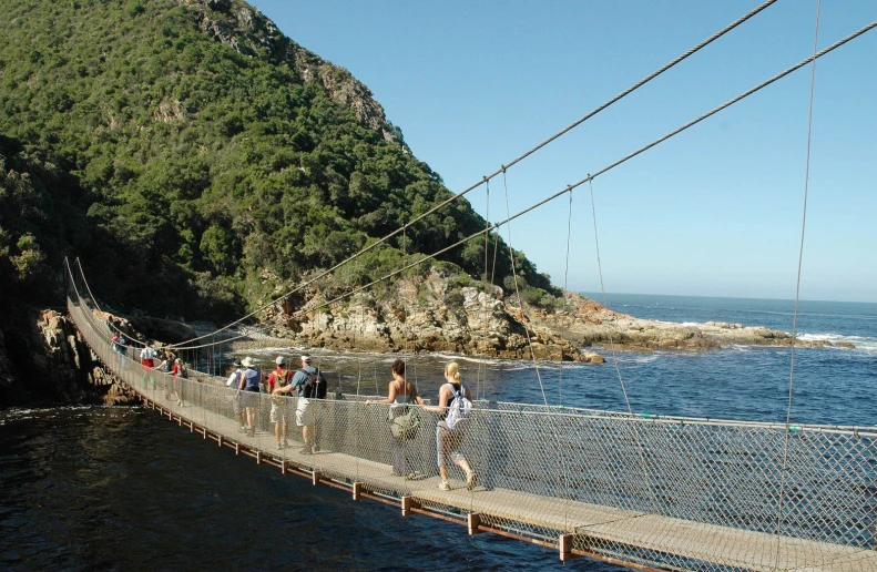 people crossing over a rope bridge that looks like it is hanging over the water