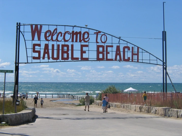 a sign in front of some ocean with people walking underneath it