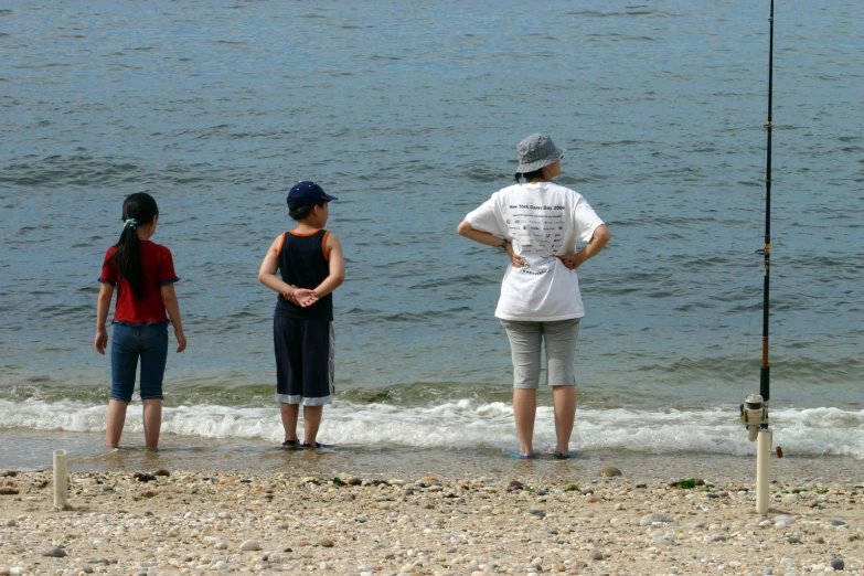 three people standing on the beach fishing from the shore