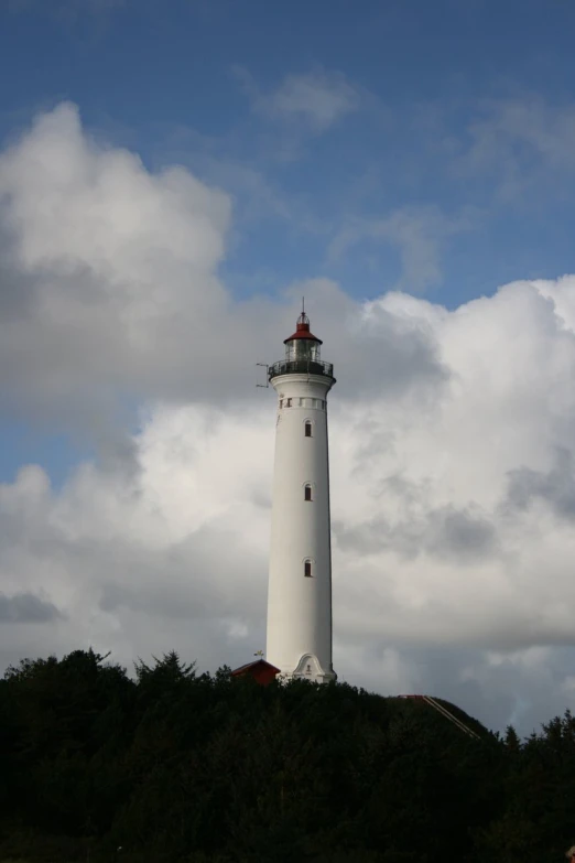 white lighthouse on a rocky hillside surrounded by cloudy skies