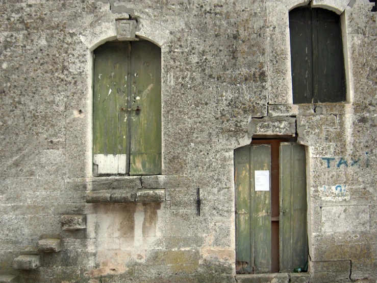 a old dilapidated stone building with two green wooden doors