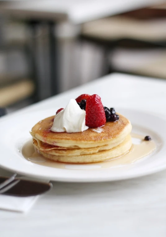 white plates with pancakes covered in fruit and whipped cream