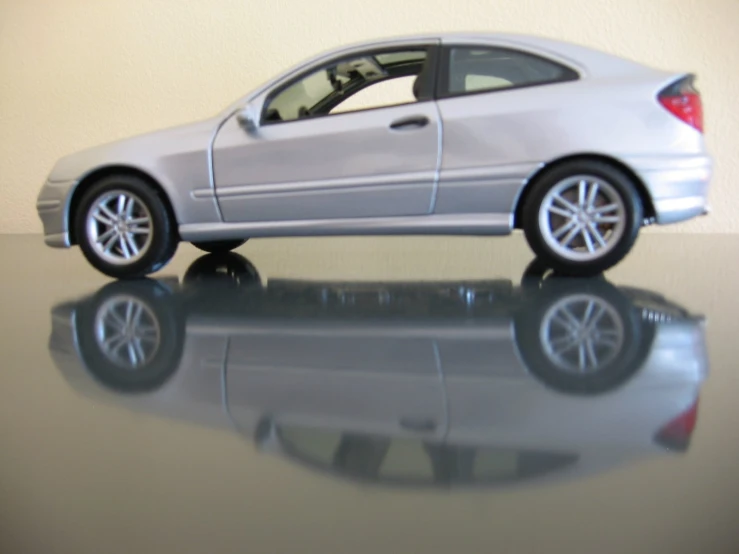 a silver toy car sitting on a reflective surface