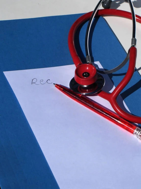 red medical stethoscope on top of white paper next to red pen