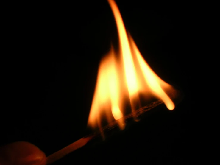 a hand holding a matchstick that is blazing in the dark