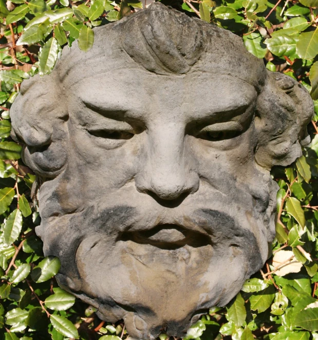 an old statue sitting among green plants