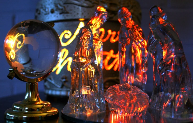 christmas figurines are sitting on a table next to the lighted globe