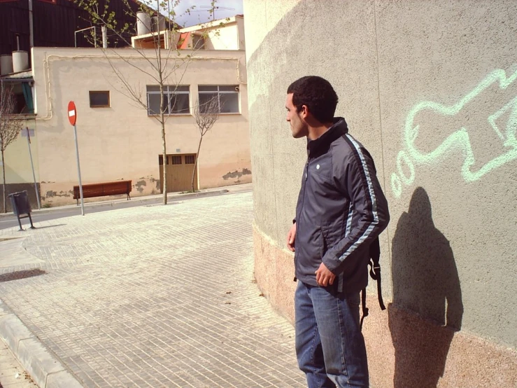 man in blue jeans and a jacket standing by a wall