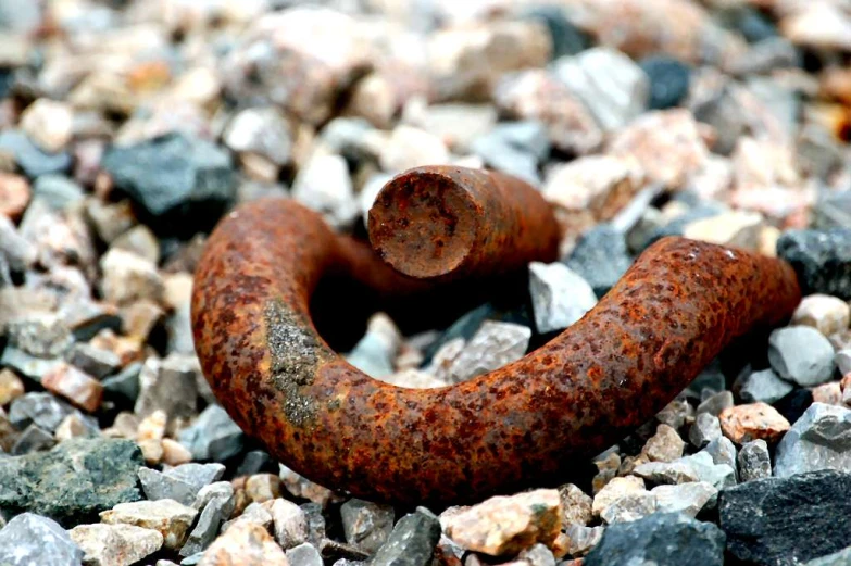 a rusted metal pipe lays on top of some rock