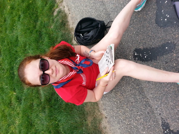 a girl in red shirt sitting on cement with skate board