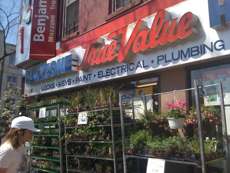 a woman in white hat walking past a flower shop