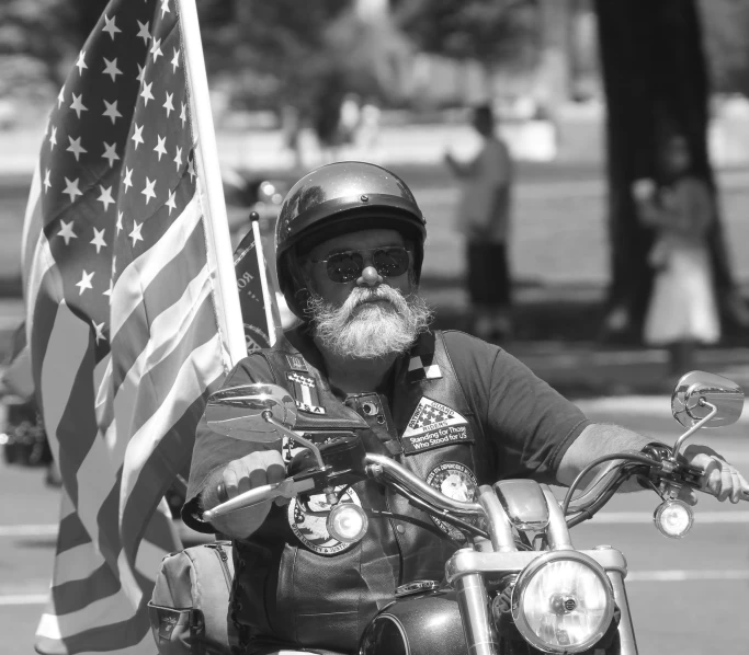 an old man riding a motorcycle holding an american flag