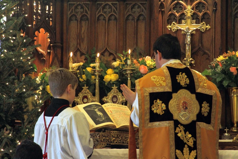 a priest wearing a red robe and other people and a christmas tree