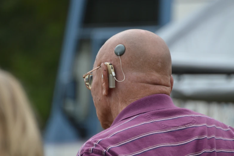 the back of a bald man wearing sunglasses and a headset