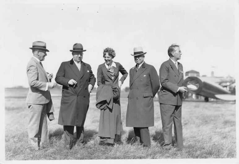 five people standing in front of an airplane with two men and one women in long suits and ties