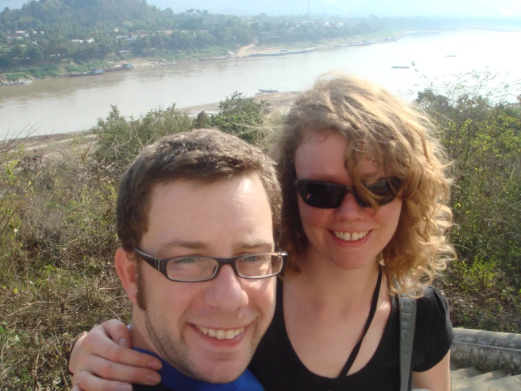 a smiling man and woman emcing near a river