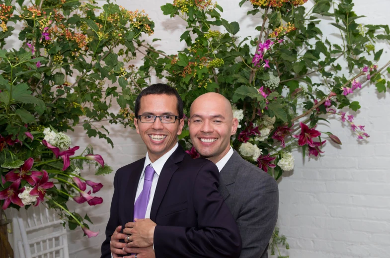 two men standing next to each other near some flowers