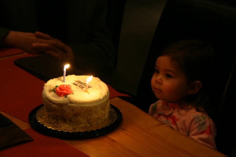 small girl looks at birthday cake with two candles